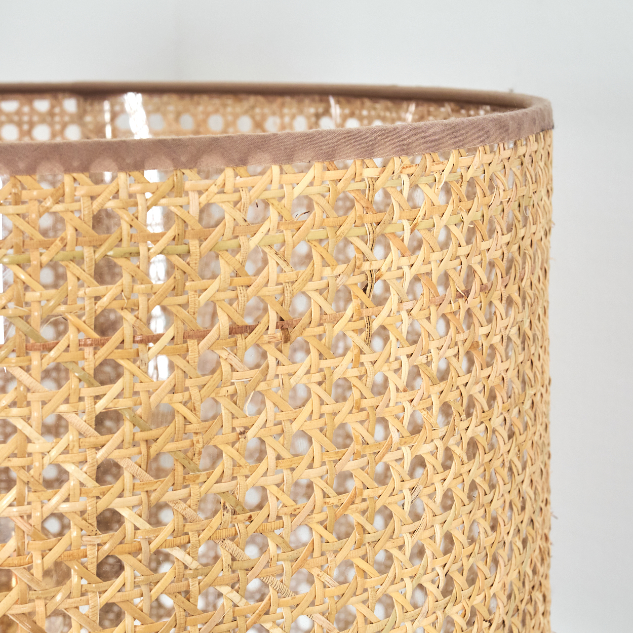 Nahaufnahme eines Lampenschirms. Er hat ein gewebtes Rattan-Design. Die Oberseite hat einen braunen Stoffbesatz. Der Hintergrund ist weiß.