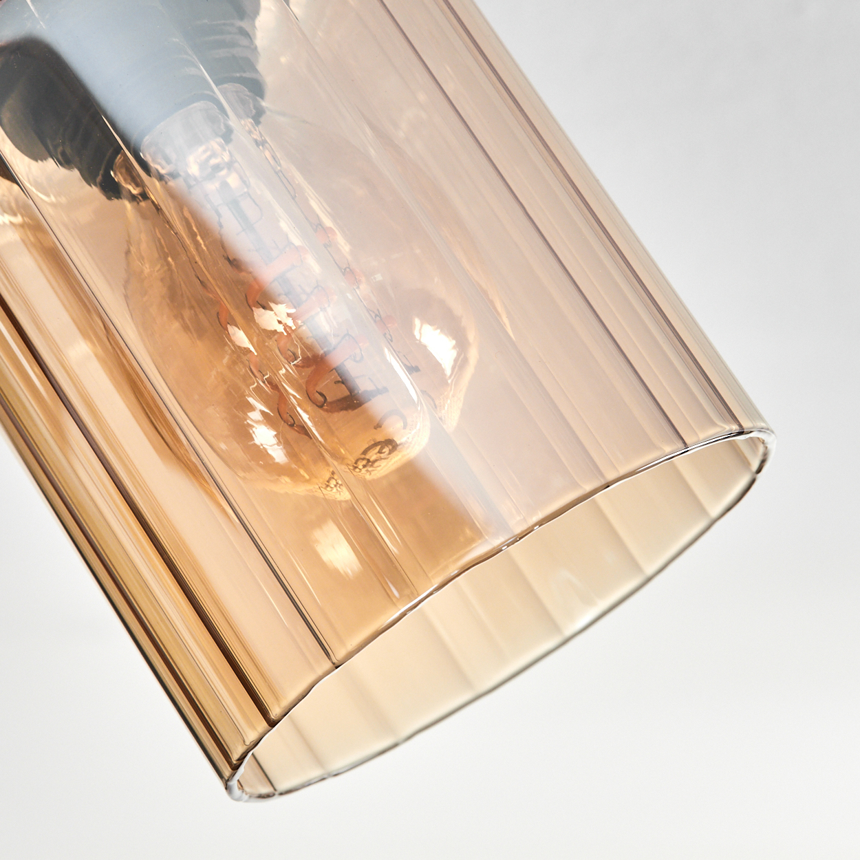 Nahaufnahme einer Leuchte. Eine klare Glühbirne befindet sich in einem gerippten bernsteinfarbenen Glasschirm. Der Hintergrund ist weiß.