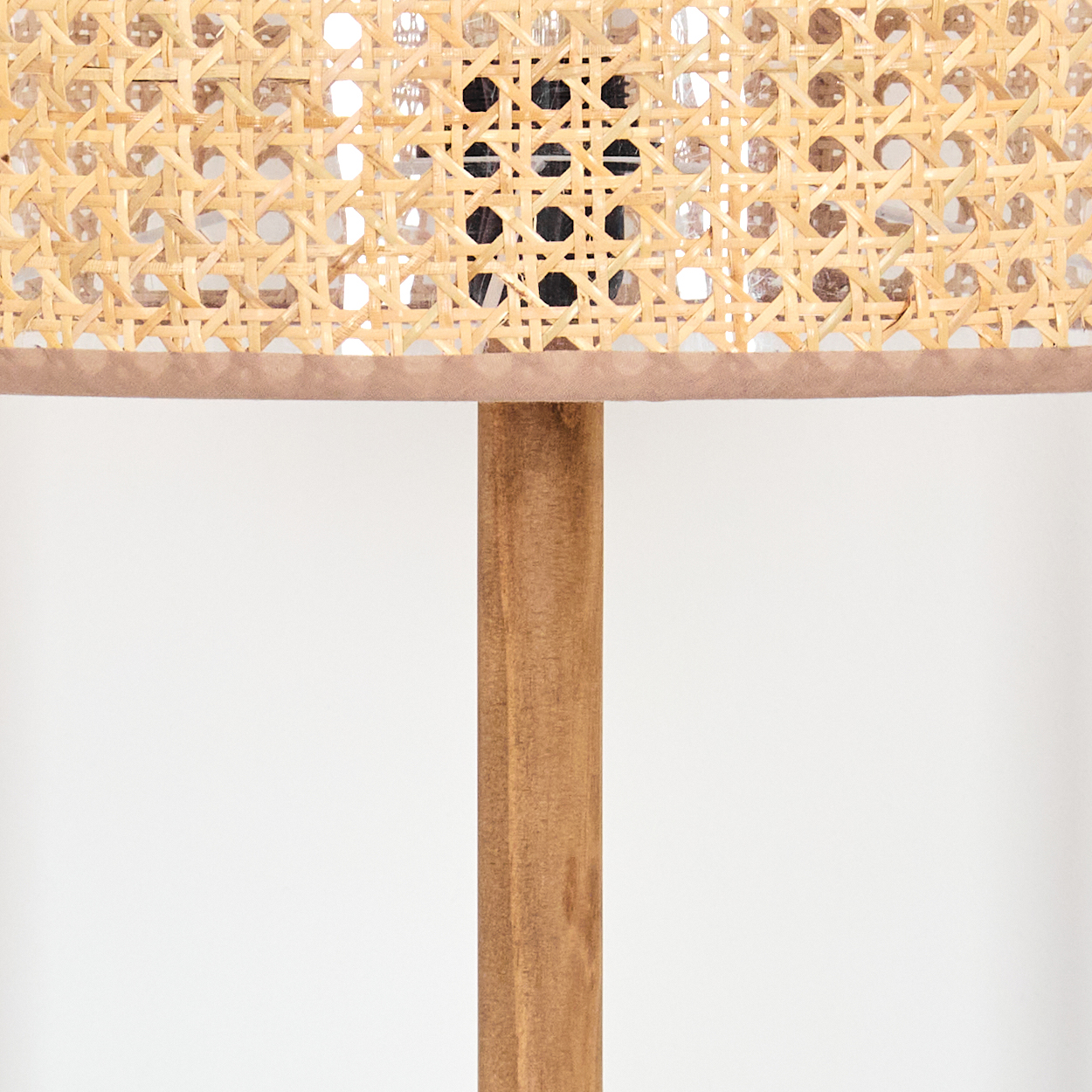 Nahaufnahme einer Lampe. Sie hat einen Schirm aus geflochtenem Rattan und einen Holzfuß. Der Hintergrund ist weiß.