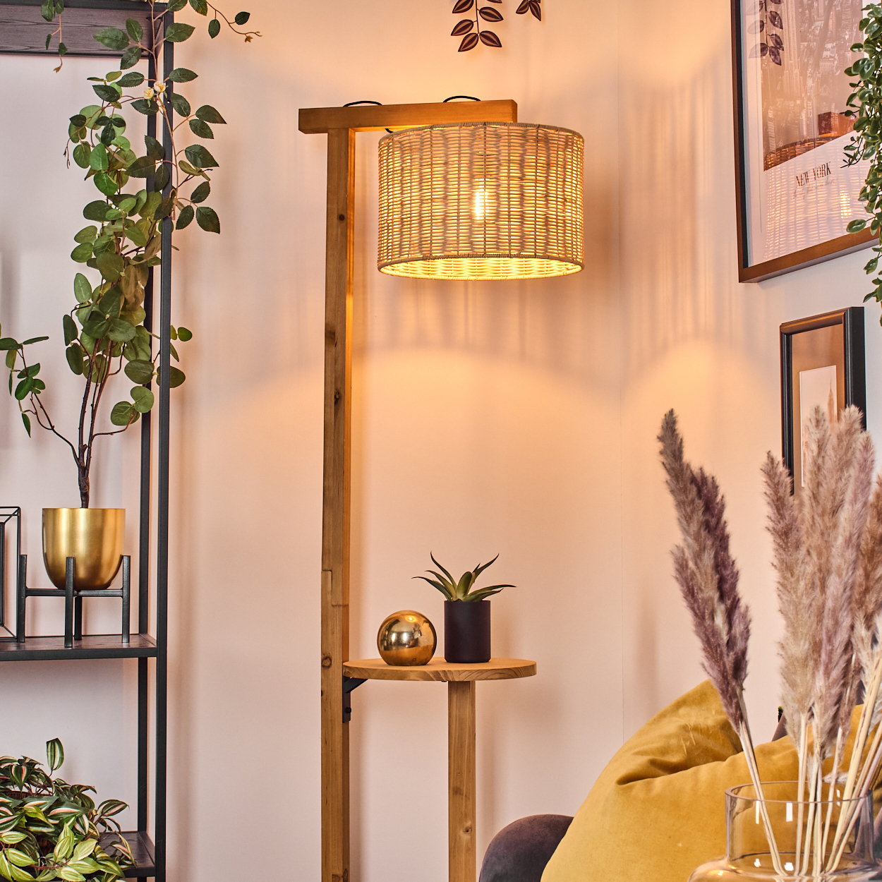 Eine Holzstehlampe mit gewebtem Lampenschirm, neben einem Regal mit Pflanzen und einer dekorativen Kugel. Ein gelbes Kissen ist sichtbar.