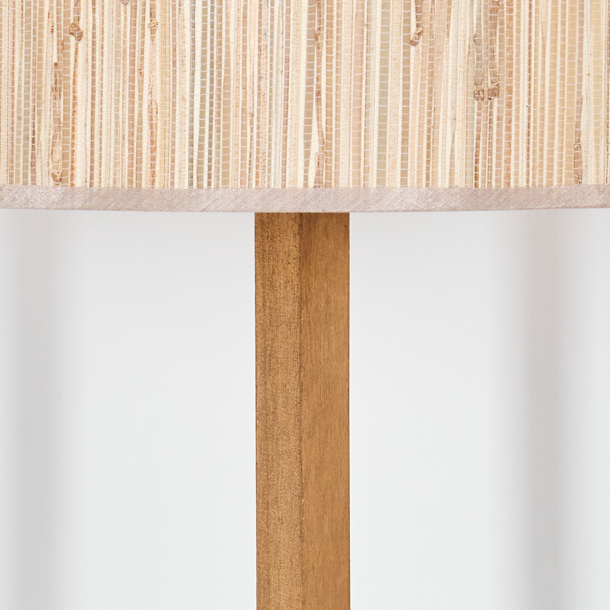Eine Lampe mit hell gewebtem Schirm und Holzstütze. Der Hintergrund ist eine schlichte weiße Fläche.