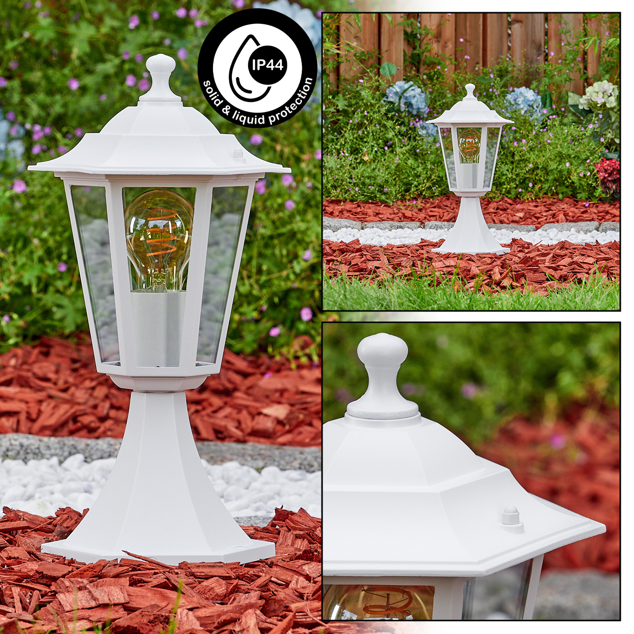 Weiße Außenlampe mit leuchtender Glühbirne, in einem Garten mit roter Mulch, weißen Steinen und grünem Laub im Hintergrund.