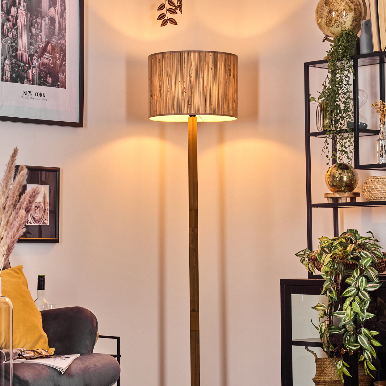 Ein Raum mit einer Stehlampe, Kunstwerken, Regalen mit Pflanzen und einem grauen Stuhl mit gelbem Kissen. Das Licht ist warm.