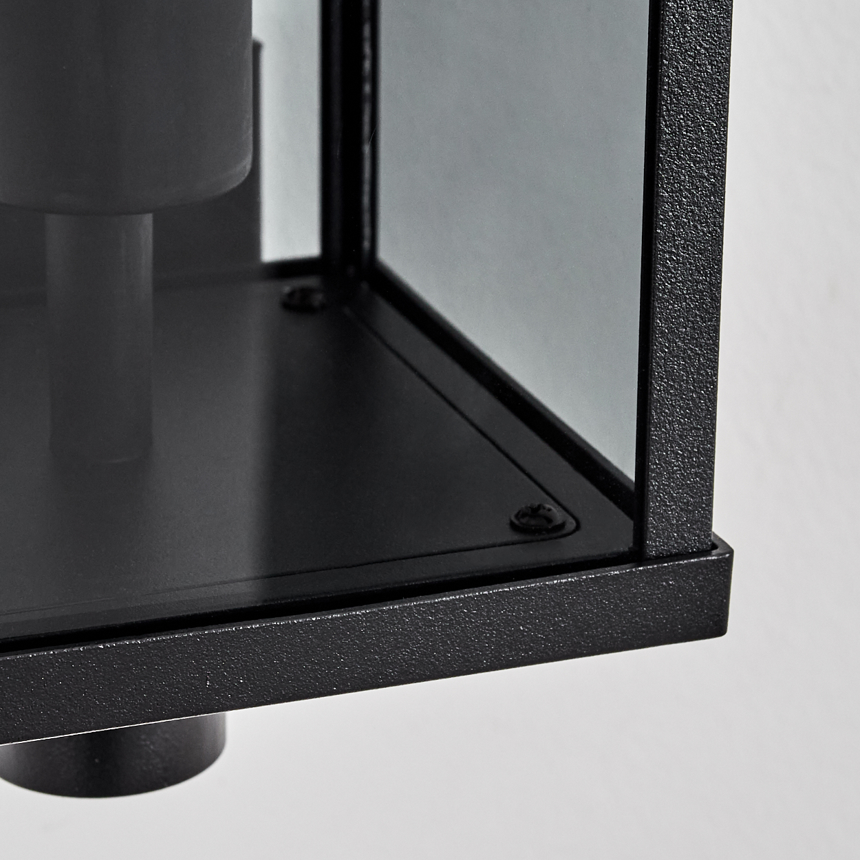 Nahaufnahme einer schwarzen Metallbox mit Glasscheiben. Ein zylindrischer Sockel trägt die Box. Schrauben sichern den Rahmen.