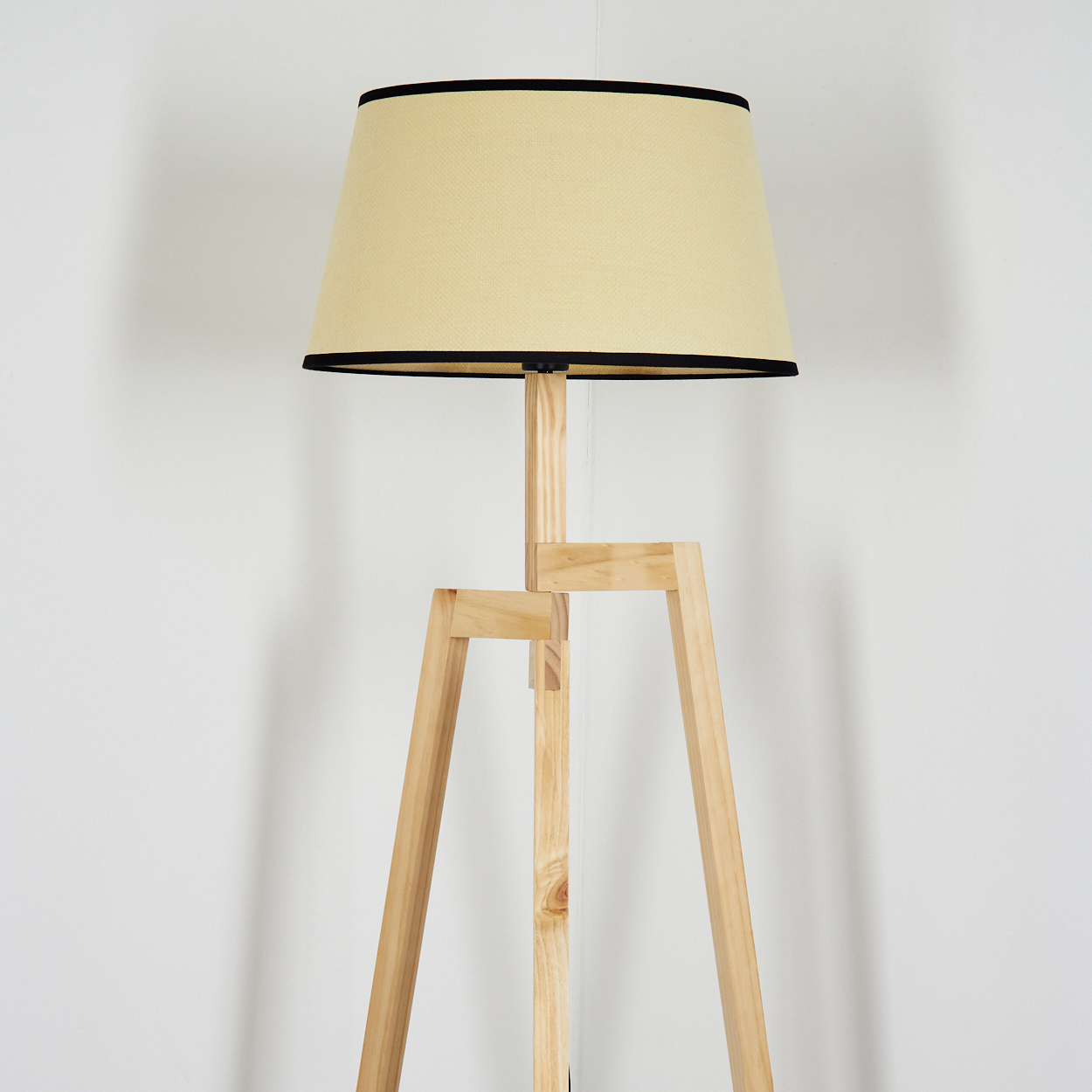 Eine Stehlampe aus Holz mit beigem Lampenschirm und schwarzem Rand vor weißer Wand.