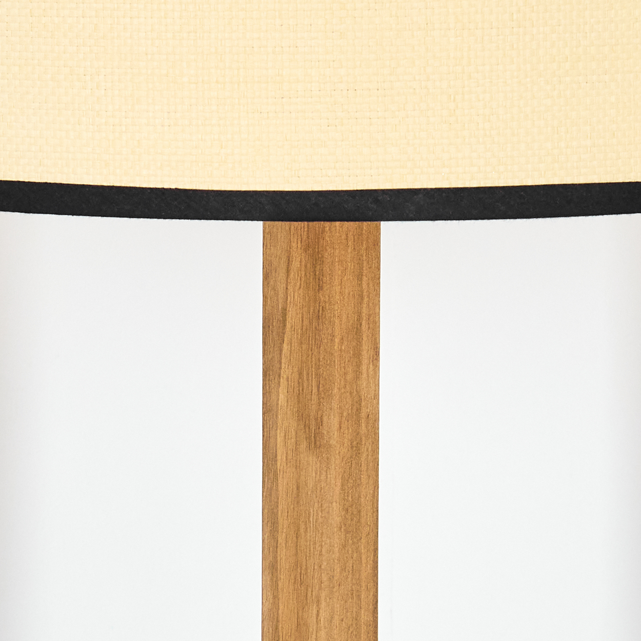 Nahaufnahme einer Lampe. Beiger Lampenschirm mit schwarzem Rand, Holzstütze in der Mitte, weißer Hintergrund.