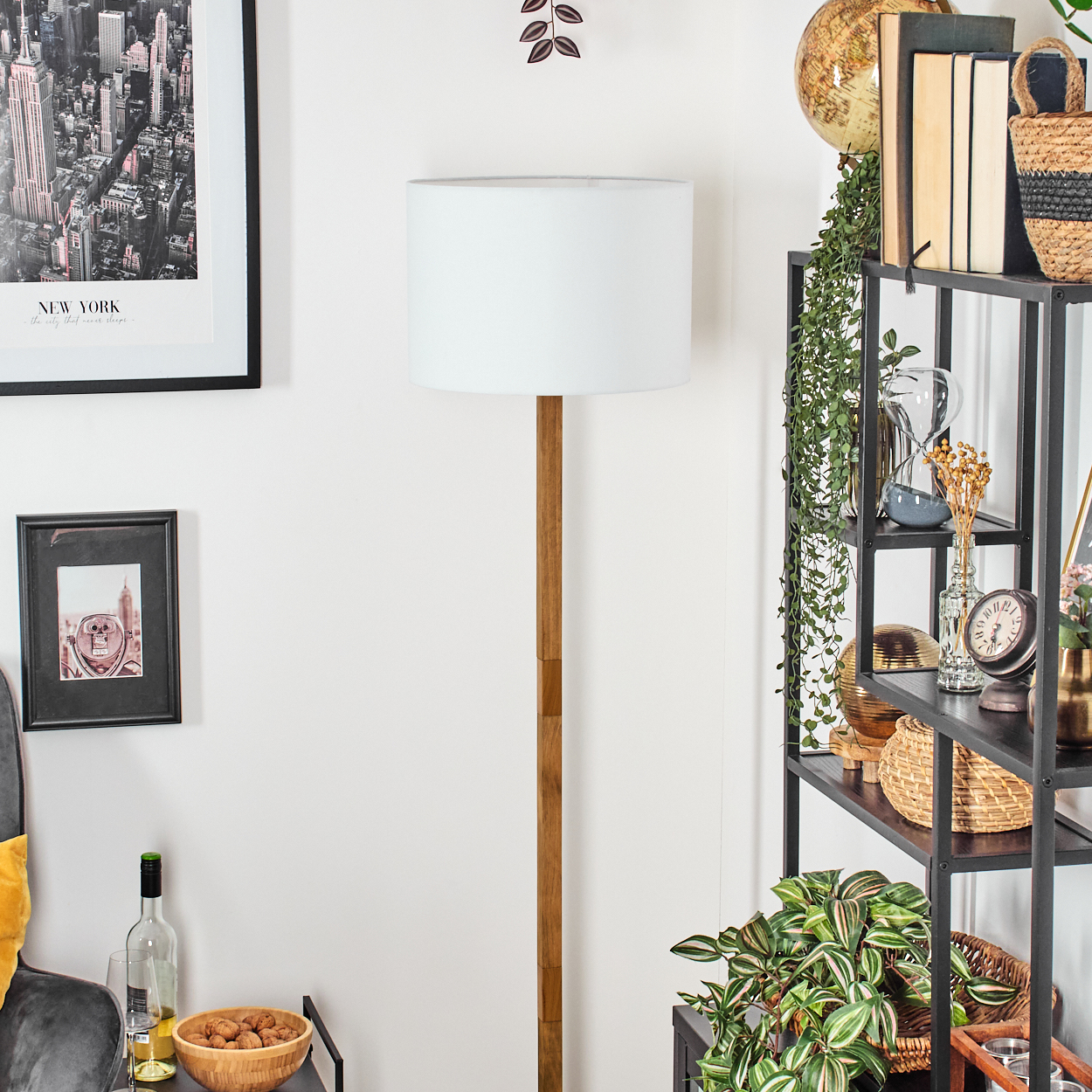 Ein Raum mit einer weißen Lampe, Bildern an der Wand und einem Regal mit Büchern und Pflanzen. Auf einem Tisch steht eine Schüssel mit Nüssen.