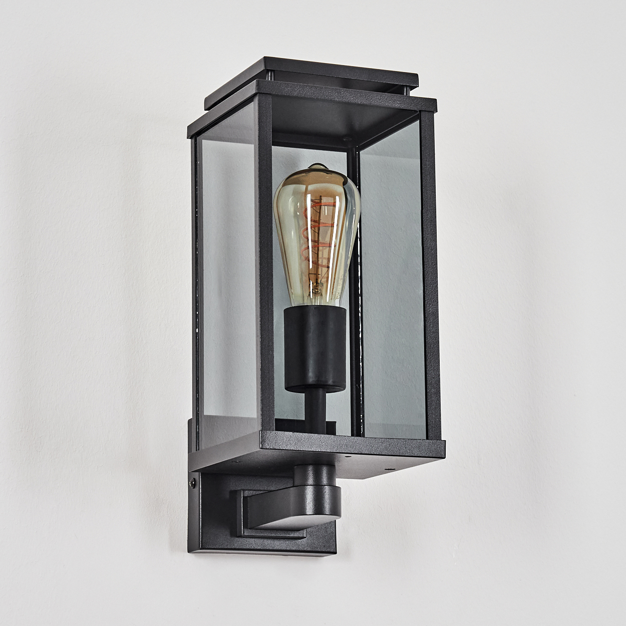Eine schwarze Außenwandleuchte mit Glasgehäuse und sichtbarer Glühbirne an einer weißen Wand.