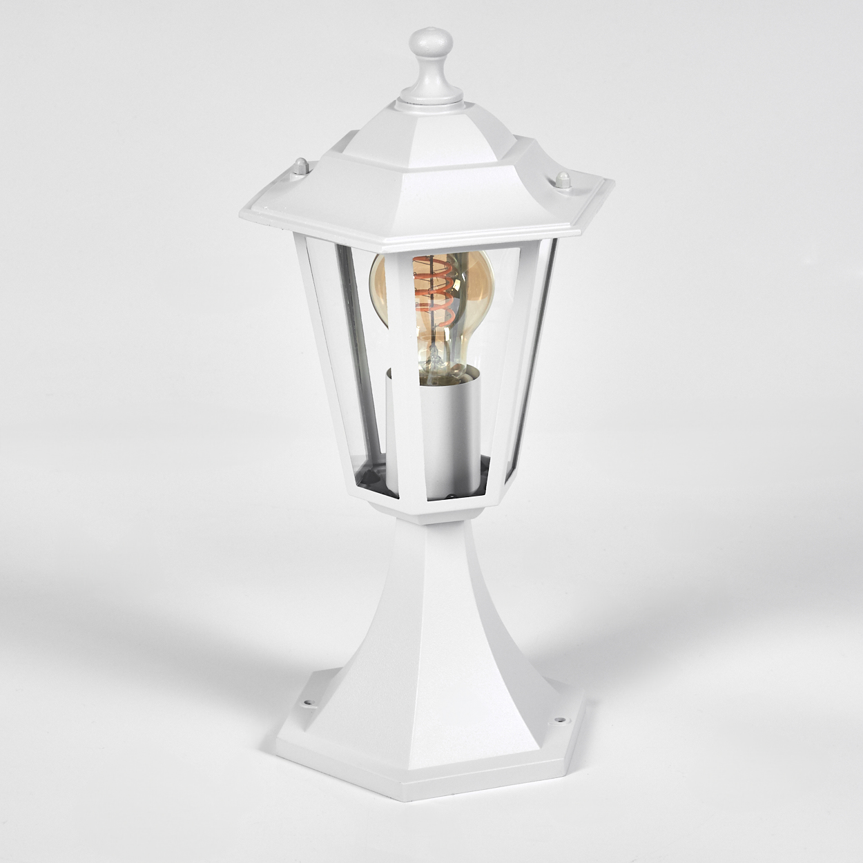 Eine weiße Außenlampe mit einer Glühbirne. Die Lampe hat einen sechseckigen Sockel und einen glaseingeschlossenen Deckel.