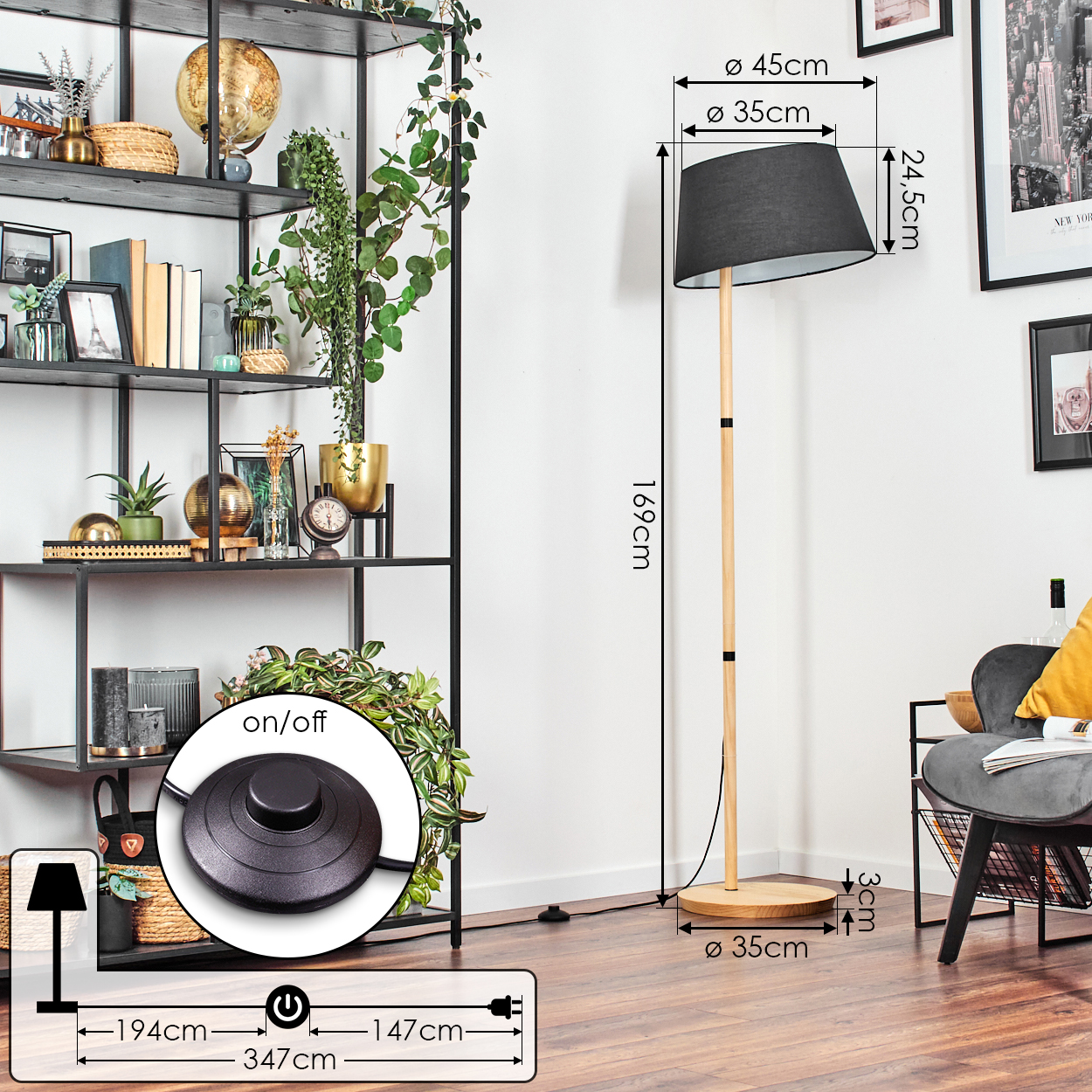 Eine Stehlampe mit schwarzem Lampenschirm steht auf einem Holzsockel. Links ein schwarzes Metallregal mit Dekorationen.