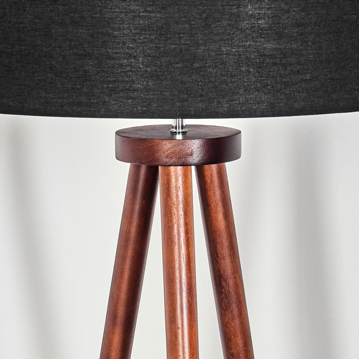 Eine hölzerne Stativlampe mit schwarzem Lampenschirm. Die Beine der Lampe sind braun, der Schirm dunkel, vor weißem Hintergrund.
