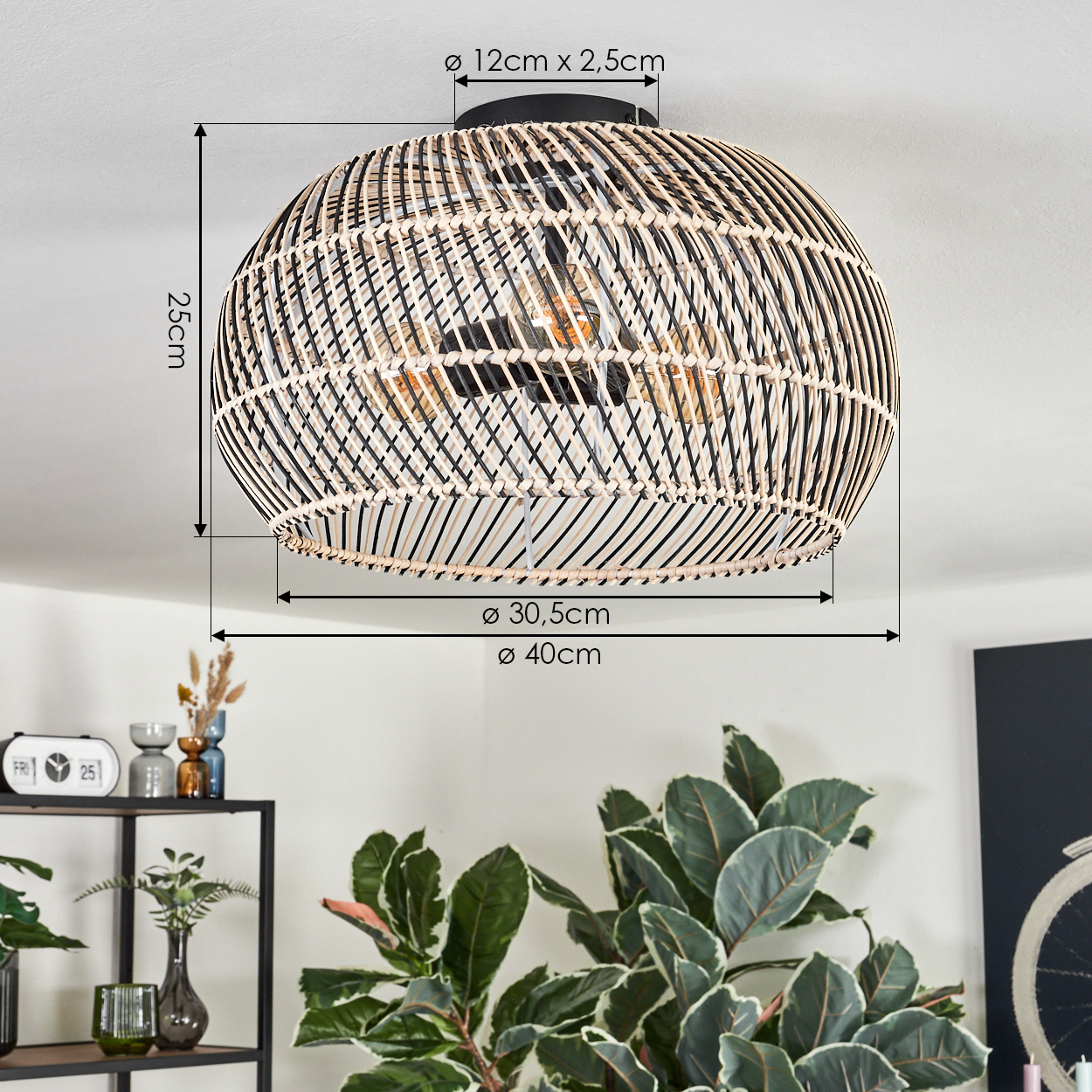 Geflochtene Rattanlampe hängt von der Decke. Ein schwarzes Metallregal mit Vasen, Pflanzen und einer Uhr ist darunter. Große grüne Pflanze rechts.