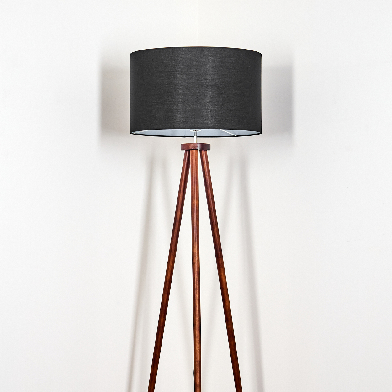 Eine Stehlampe mit schwarzem Lampenschirm und Holzstativfuß steht vor einer weißen Wand.