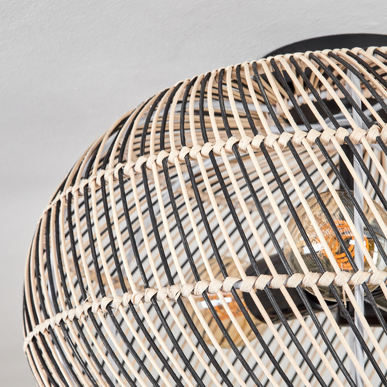 Nahaufnahme einer Rattanlampe. Die Lampe ist mit abwechselnd schwarzen und naturfarbenen Streifen gewebt. Zwei Glühbirnen sind sichtbar.