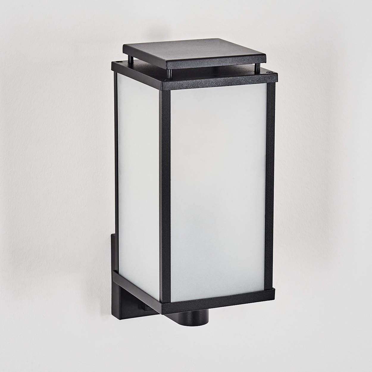 Eine schwarze, rechteckige Wandleuchte mit Milchglasscheiben. Sie ist an einer weißen Wand befestigt. Die Lampe hat eine quadratische Ober- und Unterseite.