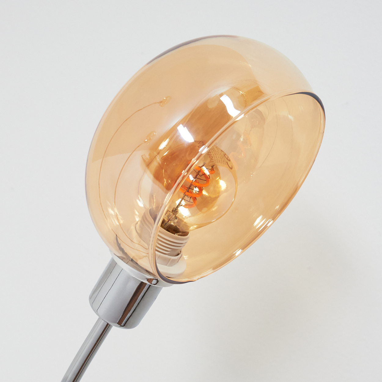 Eine moderne Lampe mit Glasschirm. Der Schirm ist bernsteinfarben und umschließt eine Glühbirne. Der Fuß und der Stiel sind metallisch.