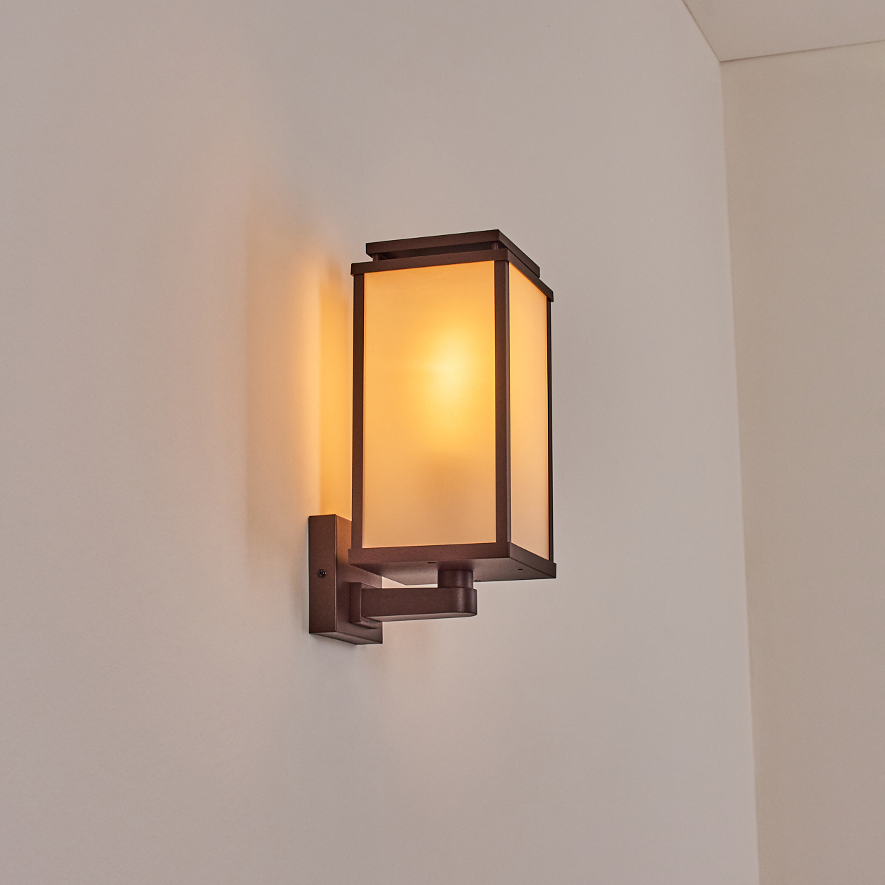 Eine rechteckige Wandleuchte mit Milchglasschirm und dunkelbraunem Rahmen ist an einer weißen Wand angebracht und leuchtet.