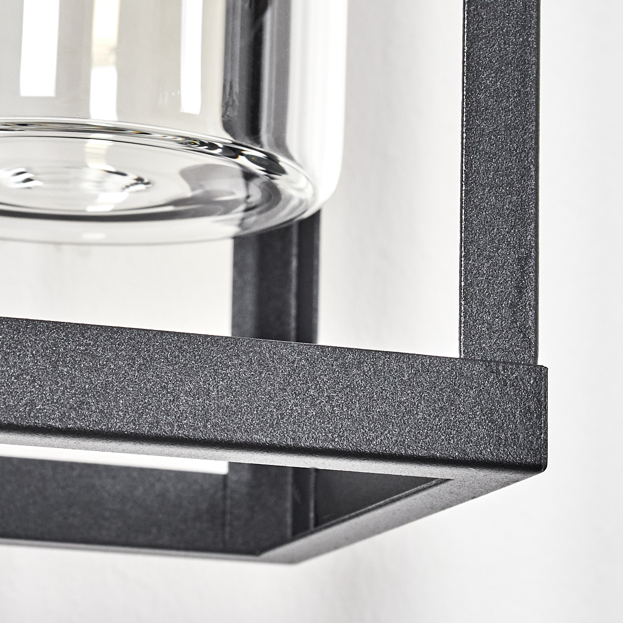 Nahaufnahme einer modernen Leuchte mit Glasschirm in einem schwarzen Metallrahmen vor einer weißen Wand.