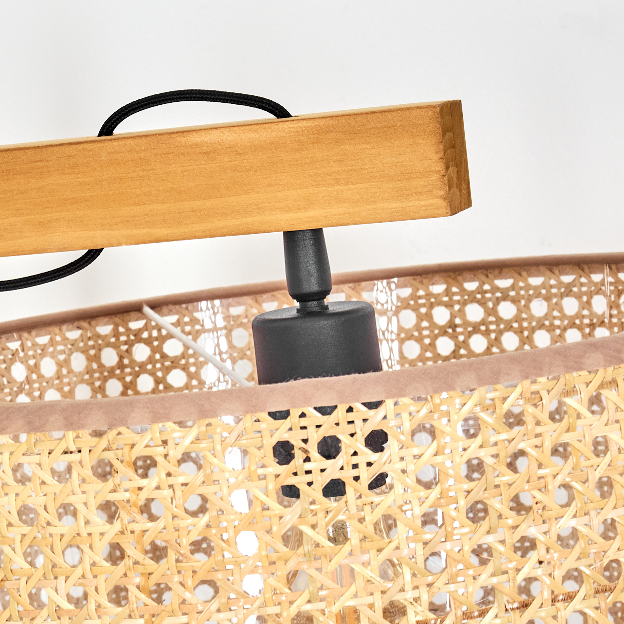 Nahaufnahme einer Lampe. Ein Holzbalken trägt eine schwarze Lampenfassung und einen gewebten Lampenschirm aus hellbraunem Material.