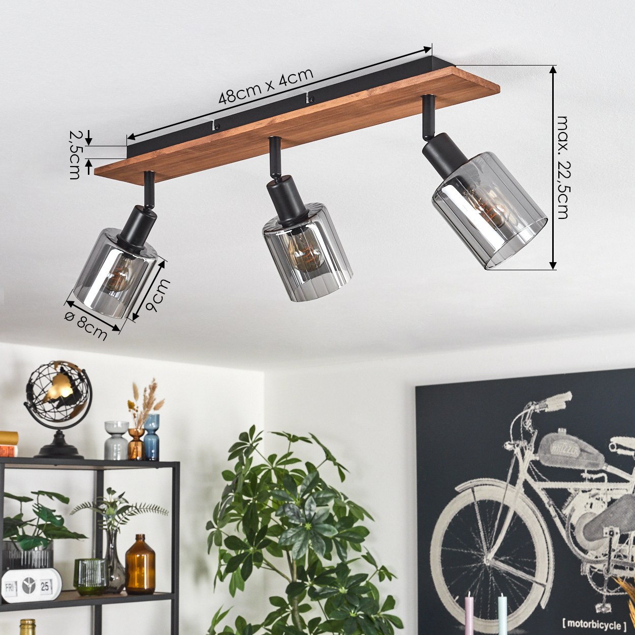 Eine Deckenlampe mit drei Strahlern. Sie hat eine Holzbasis, schwarzes Metall und graue Glasschirme. Abmessungen sind angegeben.