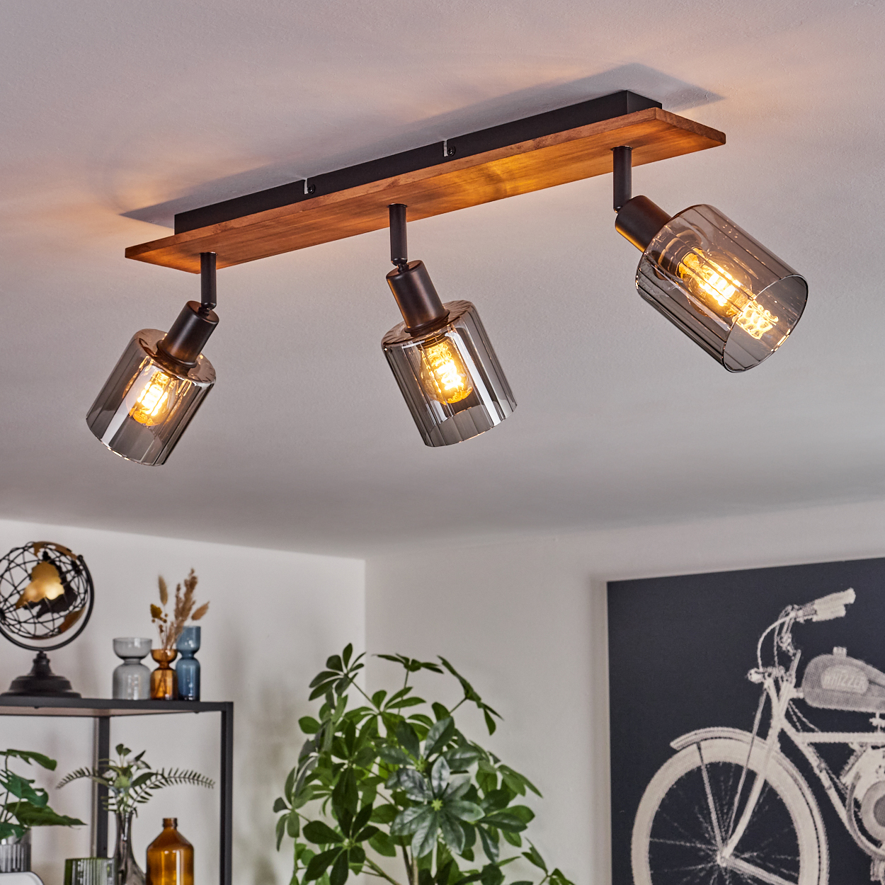 Eine Deckenleuchte mit drei Lampen. Jede Lampe hat einen rauchfarbenen Glasschirm und eine sichtbare Glühbirne, montiert auf einem Holzbalken.