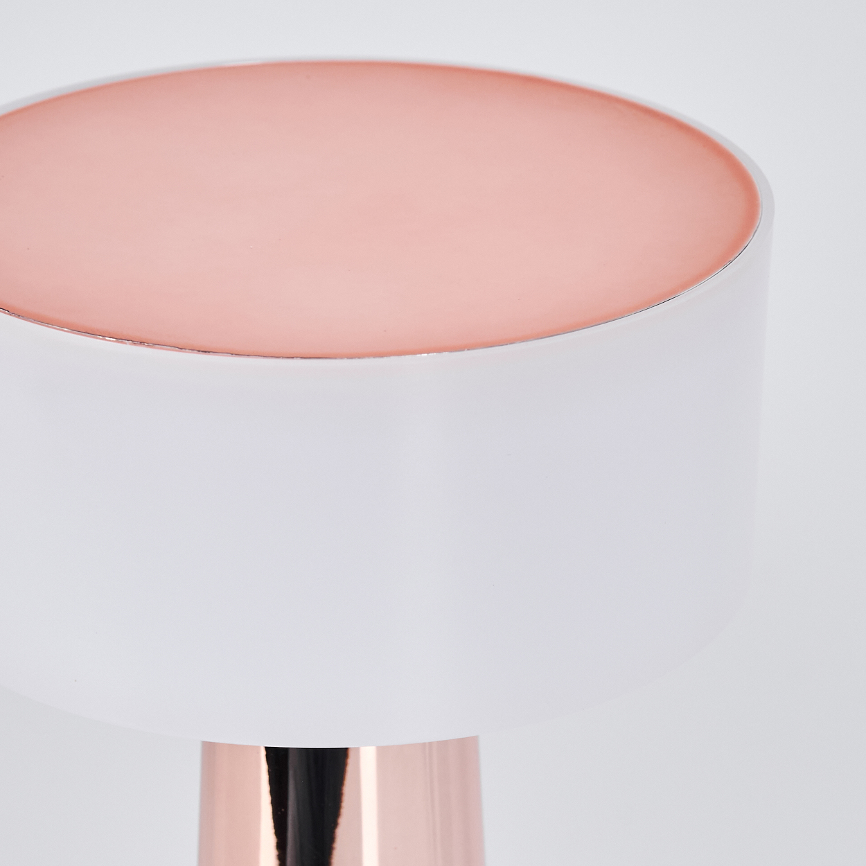 Nahaufnahme einer Lampe mit kreisförmigem rosa Oberteil und weißem Körper. Der Sockel hat eine metallische Roségoldfarbe.
