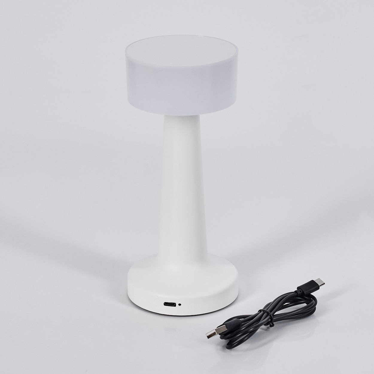 Eine weiße moderne Tischlampe mit zylindrischem Ober- und Unterteil, einem schlanken Körper und einem schwarzen USB-Kabel.