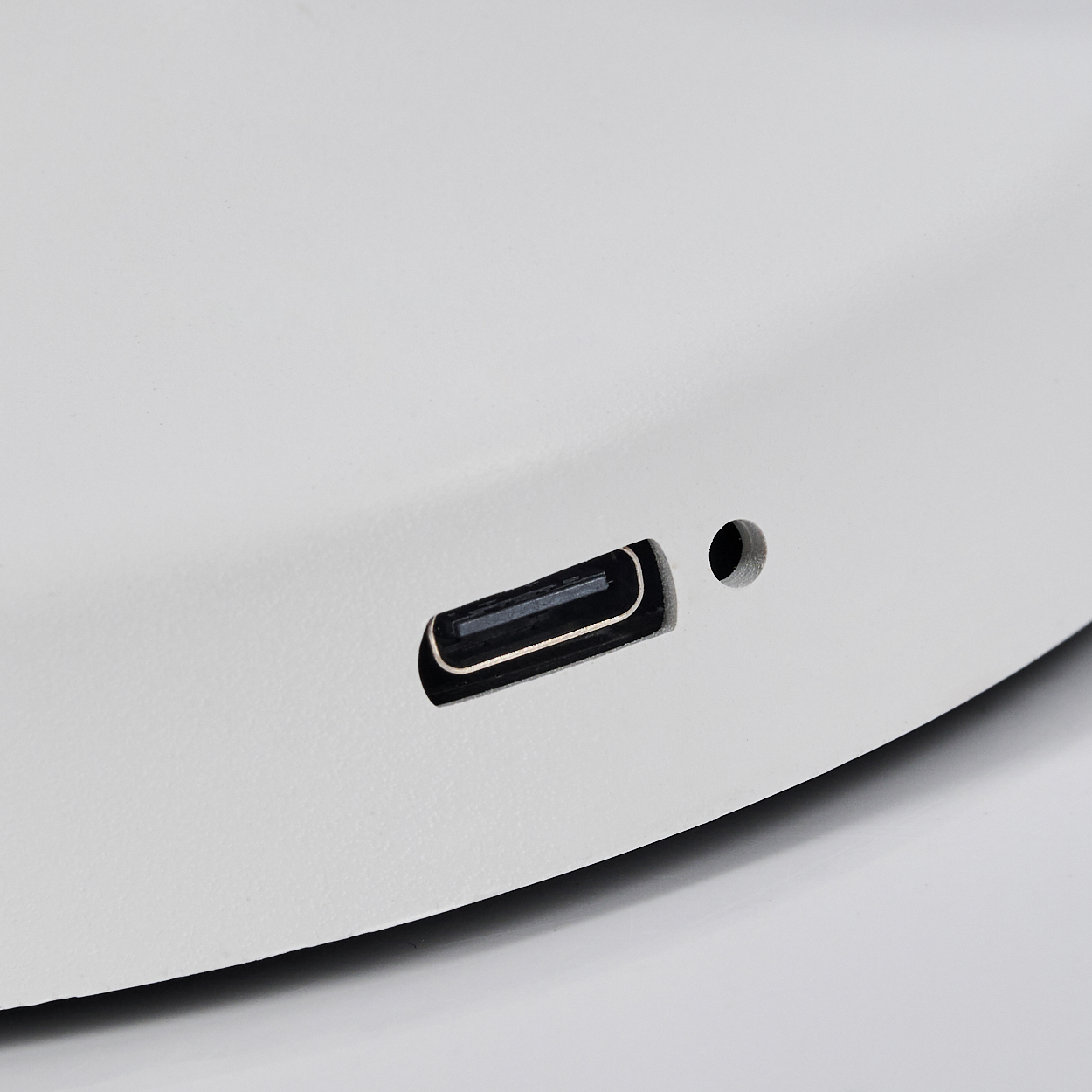 Nahaufnahme eines weißen Geräts mit USB-C-Anschluss und einem kleinen Loch. Der Anschluss ist schwarz und das Loch dunkel. Der Hintergrund ist weiß.
