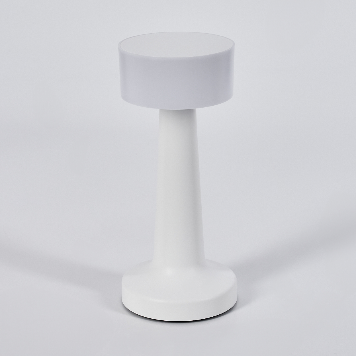 Eine weiße Lampe mit zylindrischem Oberteil und konischem Fuß steht vor weißem Hintergrund. Schatten sind zu sehen.