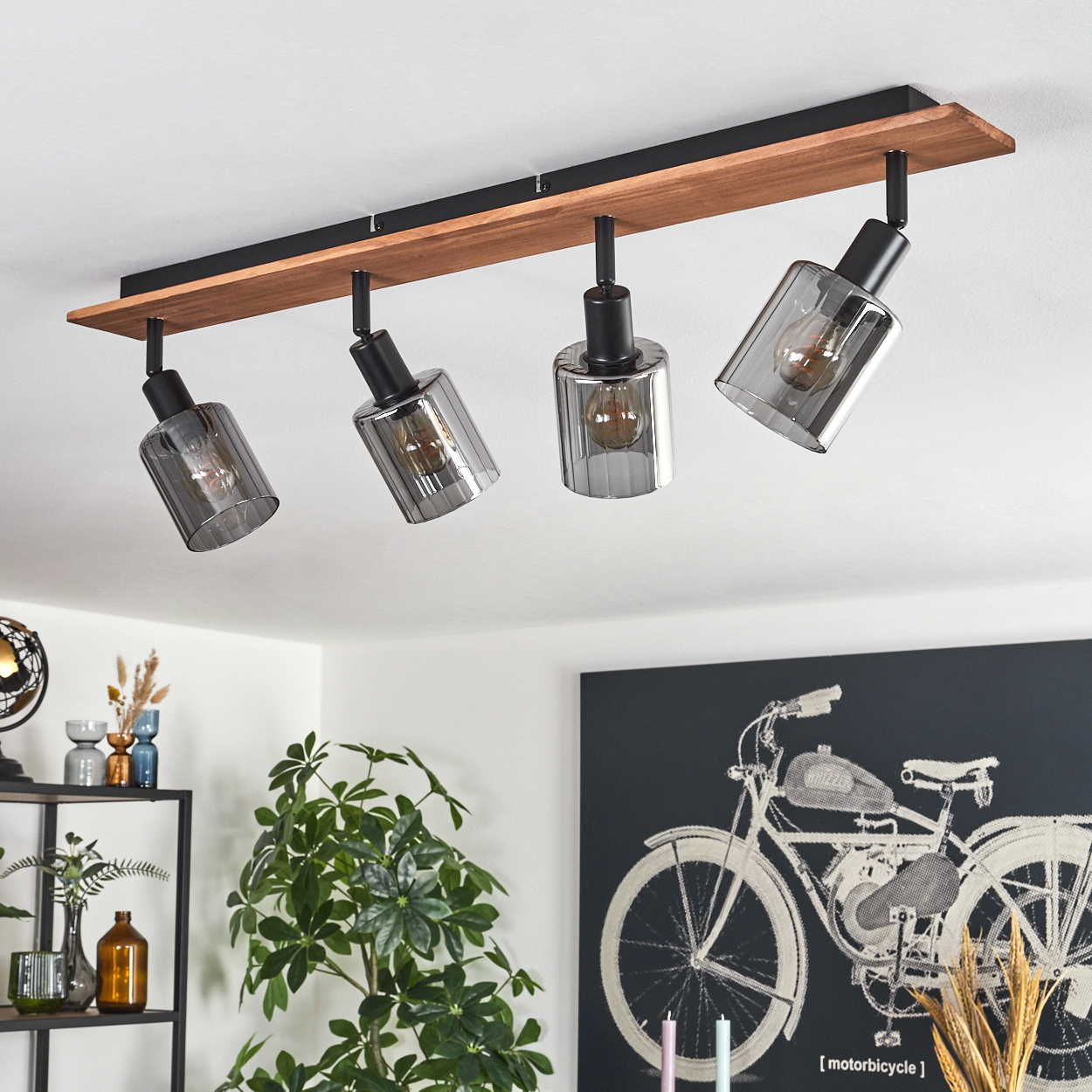 Vierflammige Leuchte an Holzbalken. Graue Glasschirme mit Glühbirnen. Ein schwarz-weißes Motorradkunstwerk an der Wand.