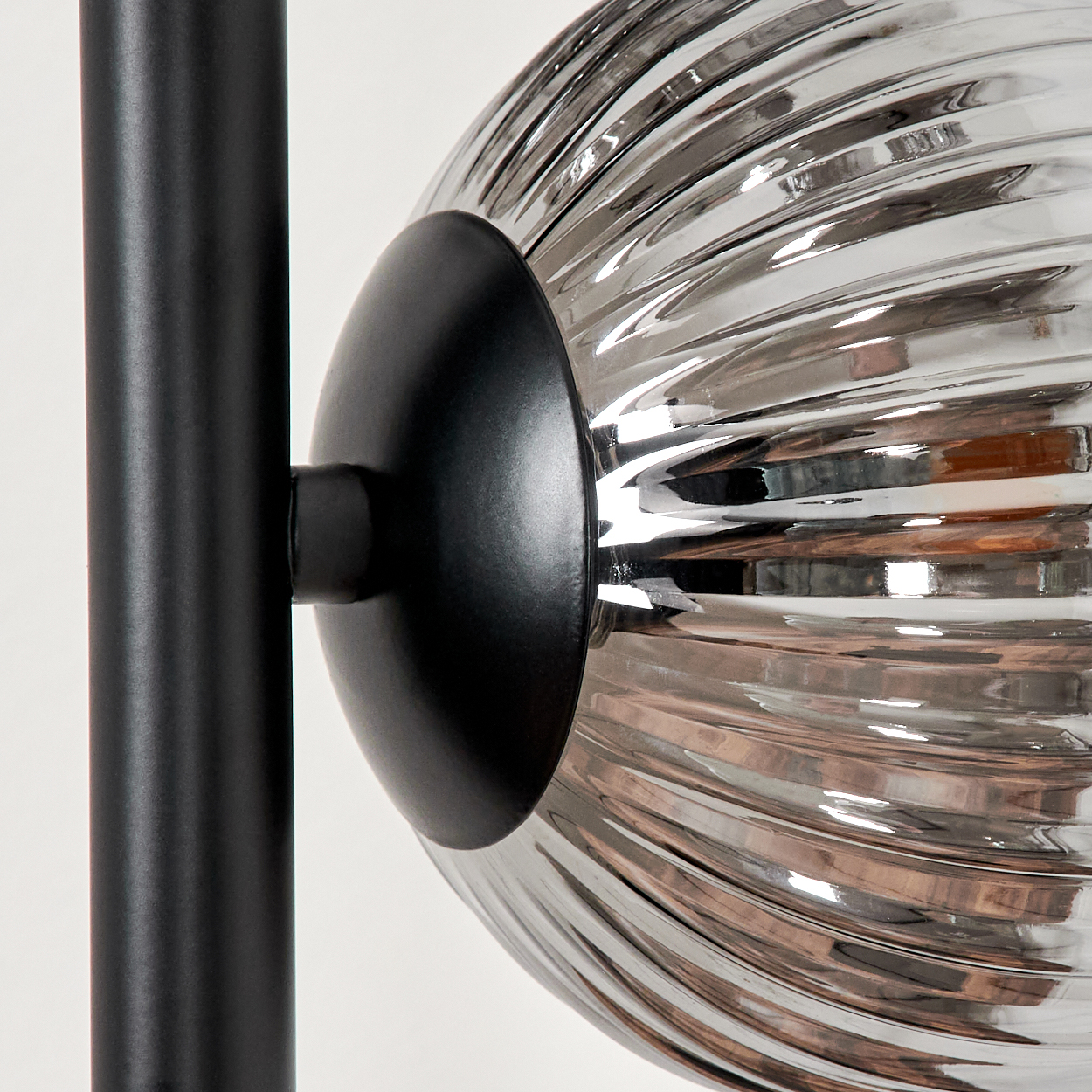 Nahaufnahme einer Lampe. Eine schwarze Metallstange trägt eine gerippte Glaskugel. Die Kugel ist durch ein schwarzes Kreisteil verbunden.