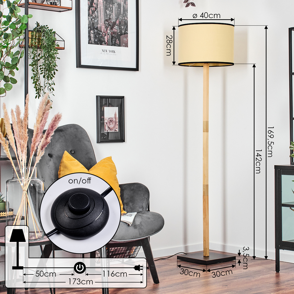 Eine Stehlampe mit beigem Lampenschirm steht neben einem grauen Sessel. Ein schwarz gerahmtes Bild hängt an der Wand.