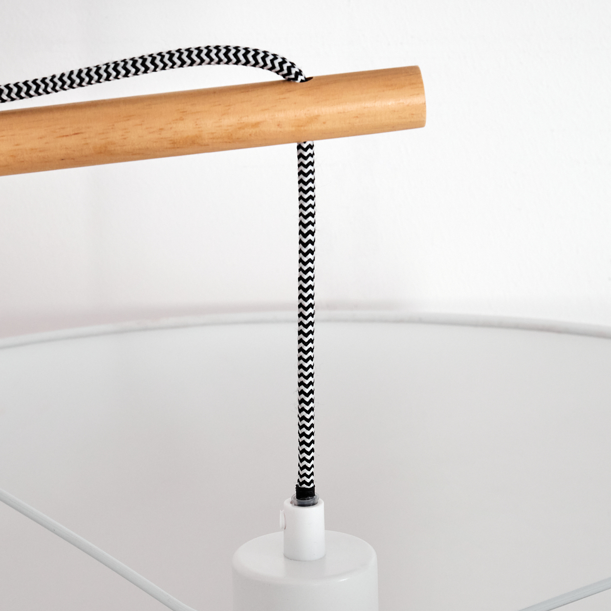 Nahaufnahme einer Lampe. Sie hat eine Holzstange, ein schwarz-weißes Zickzackmusterkabel und einen weißen Lampenschirm.