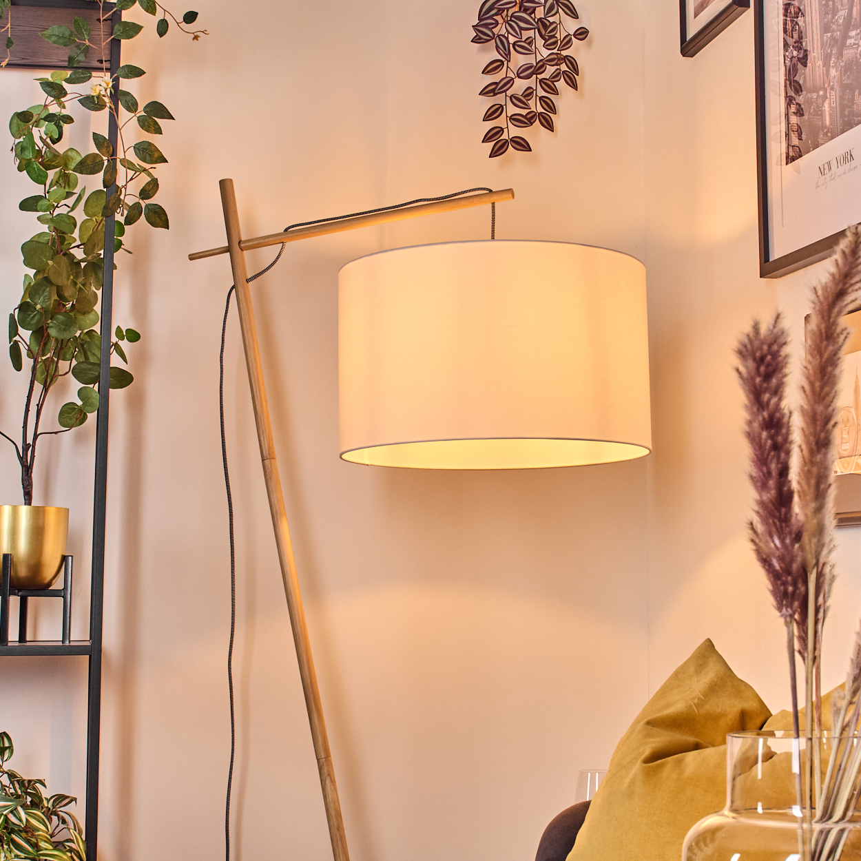Ein modernes Wohnzimmer mit einer hölzernen Stehlampe und einem weißen Lampenschirm. Pflanzen und ein goldener Topf sind im Hintergrund.