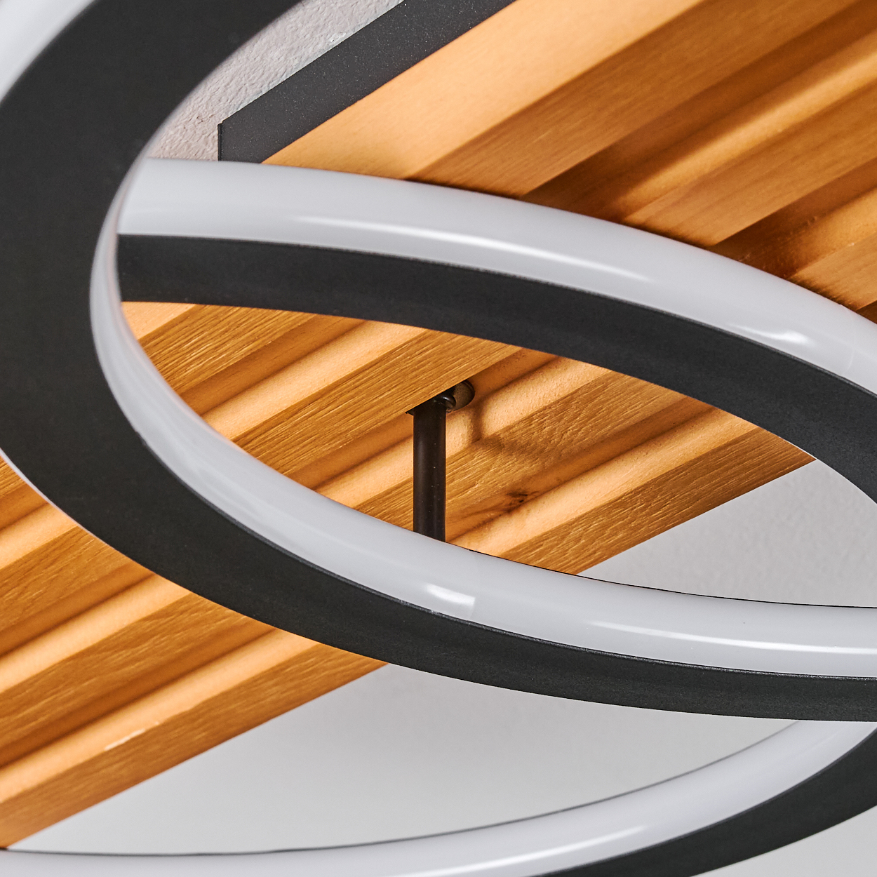 Nahaufnahme einer modernen Deckenleuchte. Sie verfügt über ein Holzlatten-Design, schwarze Ringe und weiße Neonlichtstreifen.