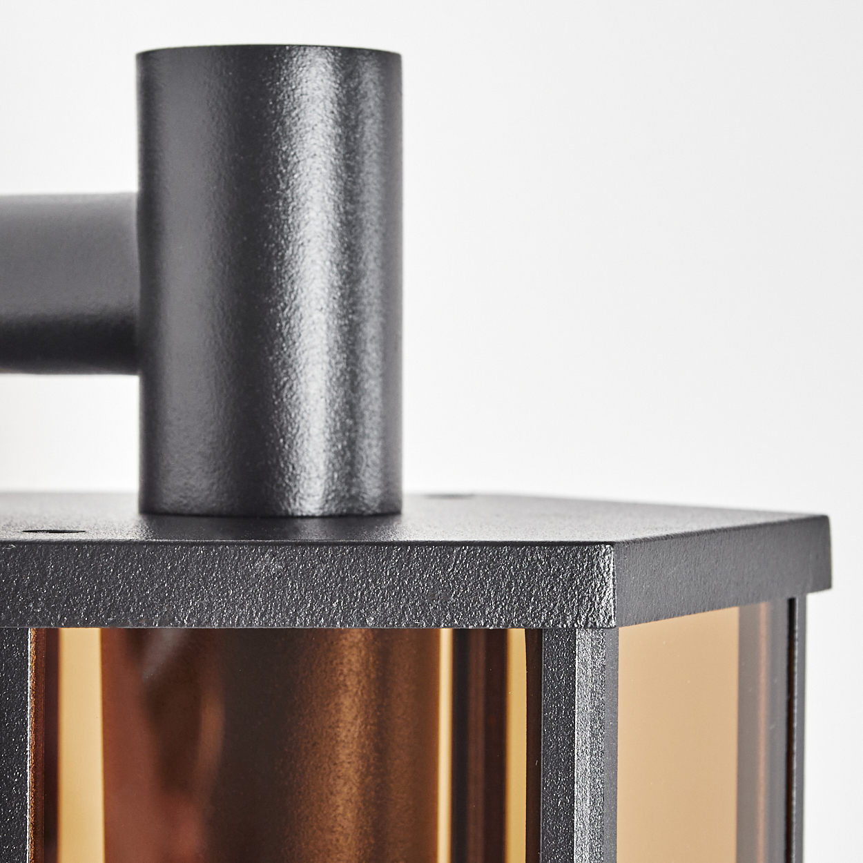 Nahaufnahme einer schwarzen Metallstruktur mit zylindrischer Oberseite und rechteckiger Basis. Eine goldbraune Glasscheibe ist sichtbar.