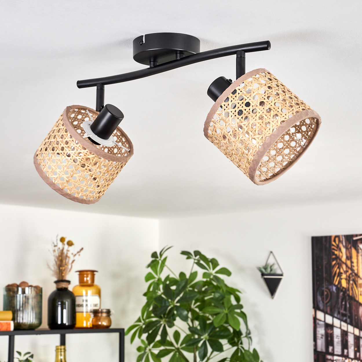 Deckenlampe mit zwei gewebten Schirmen. Unten sind Pflanzen, Vasen und ein schwarzes Regal. Im Hintergrund sind ein Gemälde und ein Wandpflanzer.