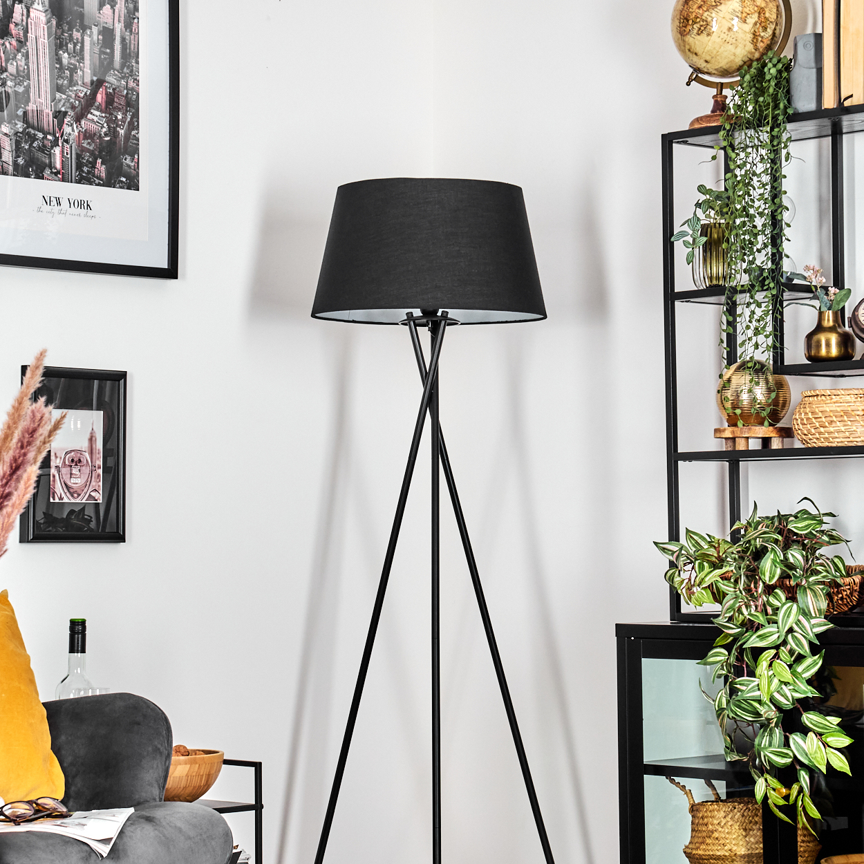Eine schwarze Stehlampe steht in einem Raum mit einem New York-Poster und einem Bücherregal mit Pflanzen und Dekoration.