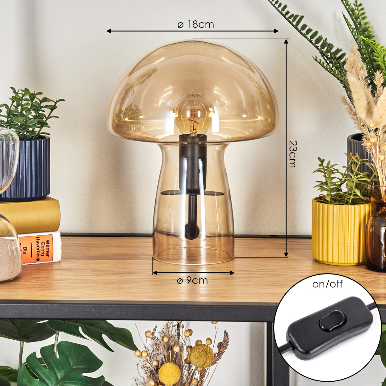 Eine pilzförmige Lampe mit Glühbirne. Die Lampe steht auf einem Holzregal mit Pflanzen und einem Schalter mit der Aufschrift 'ein/aus'.