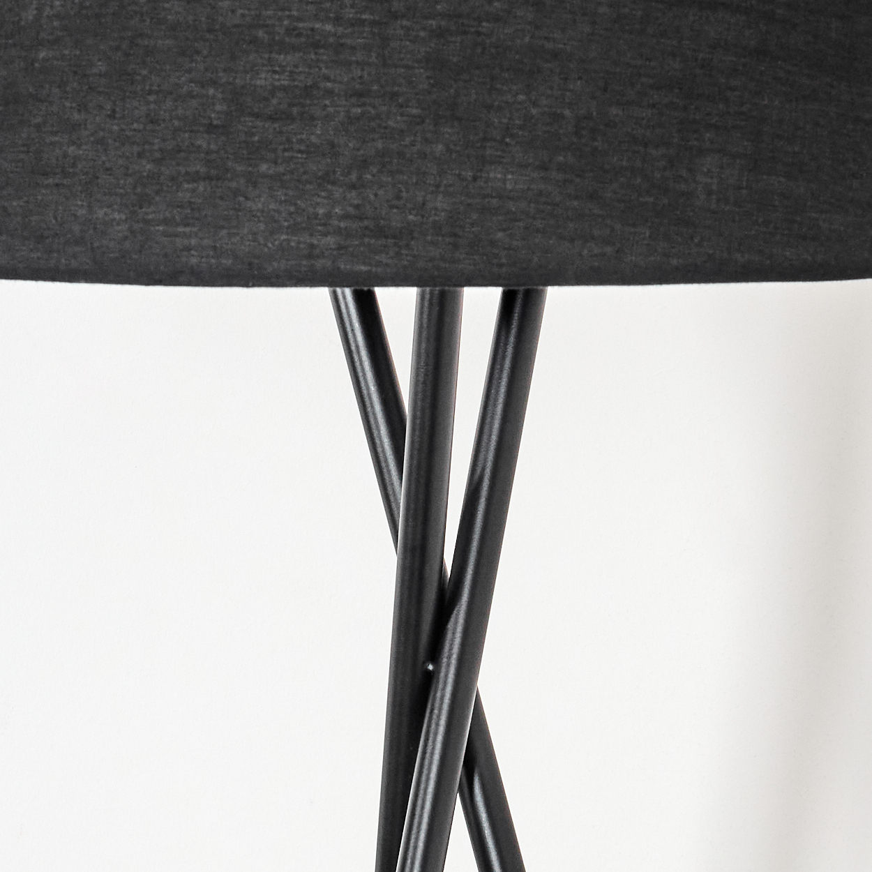 Nahaufnahme einer schwarzen Lampe. Der Lampenschirm befindet sich oben und die schwarzen Beine in der Mitte. Der Hintergrund ist eine weiße Wand.