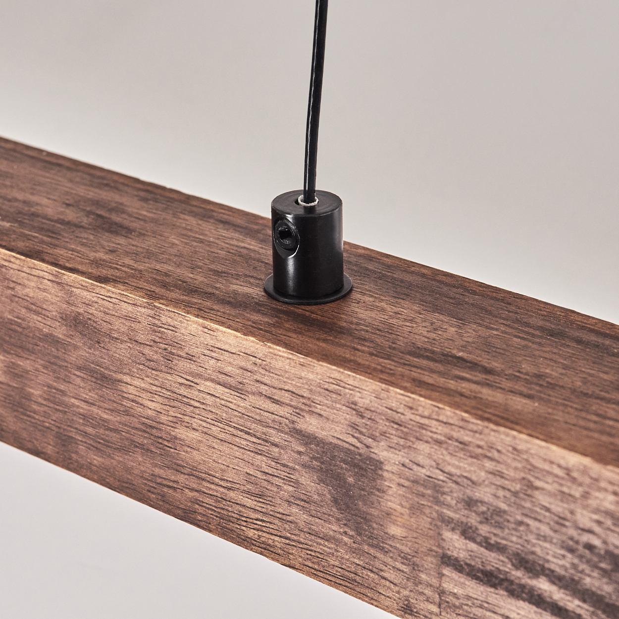 Nahaufnahme eines Holzbalkens mit schwarzem Kabel und Halterung. Das Holz ist braun, der Hintergrund ist schlicht.