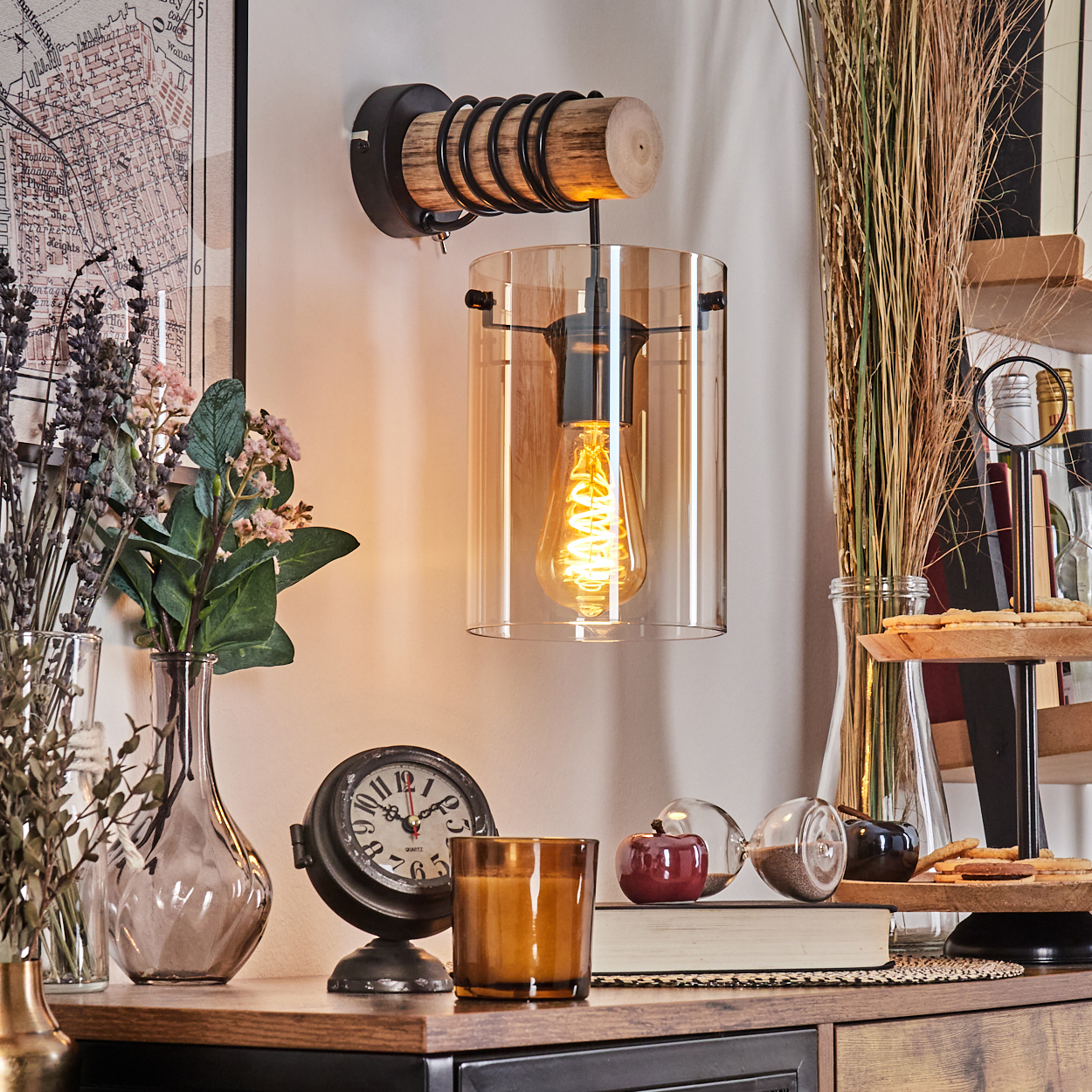 Eine beleuchtete Wandlampe im Vintage-Stil mit klarem Glasschirm. Weitere Objekte sind Vasen mit Blumen, eine Uhr, Kerzen und Dekorationen.