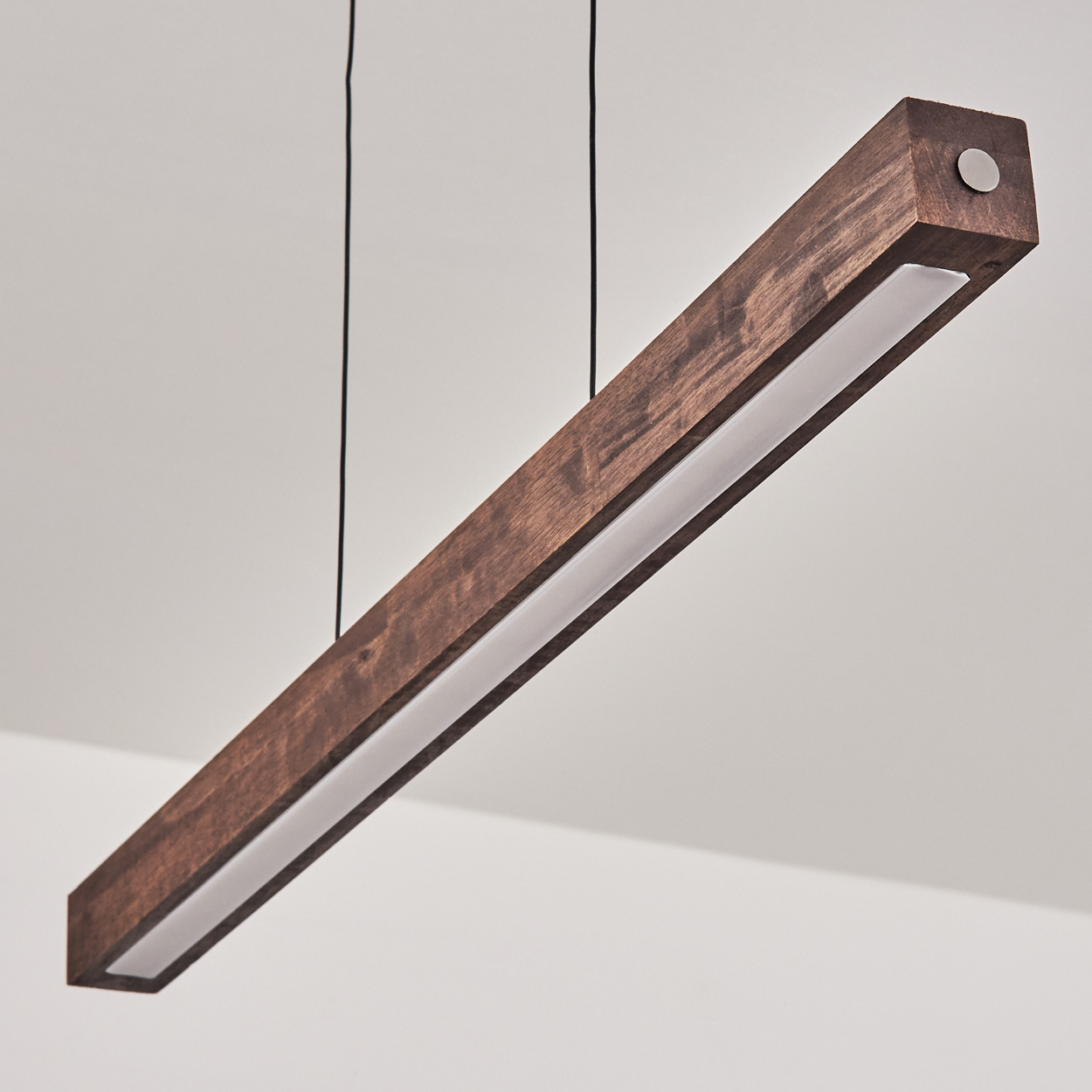 Eine rechteckige Holzleuchte, die von der Decke hängt. Sie ist braun mit einem weißen Lichtstreifen und einem Metallknopf.