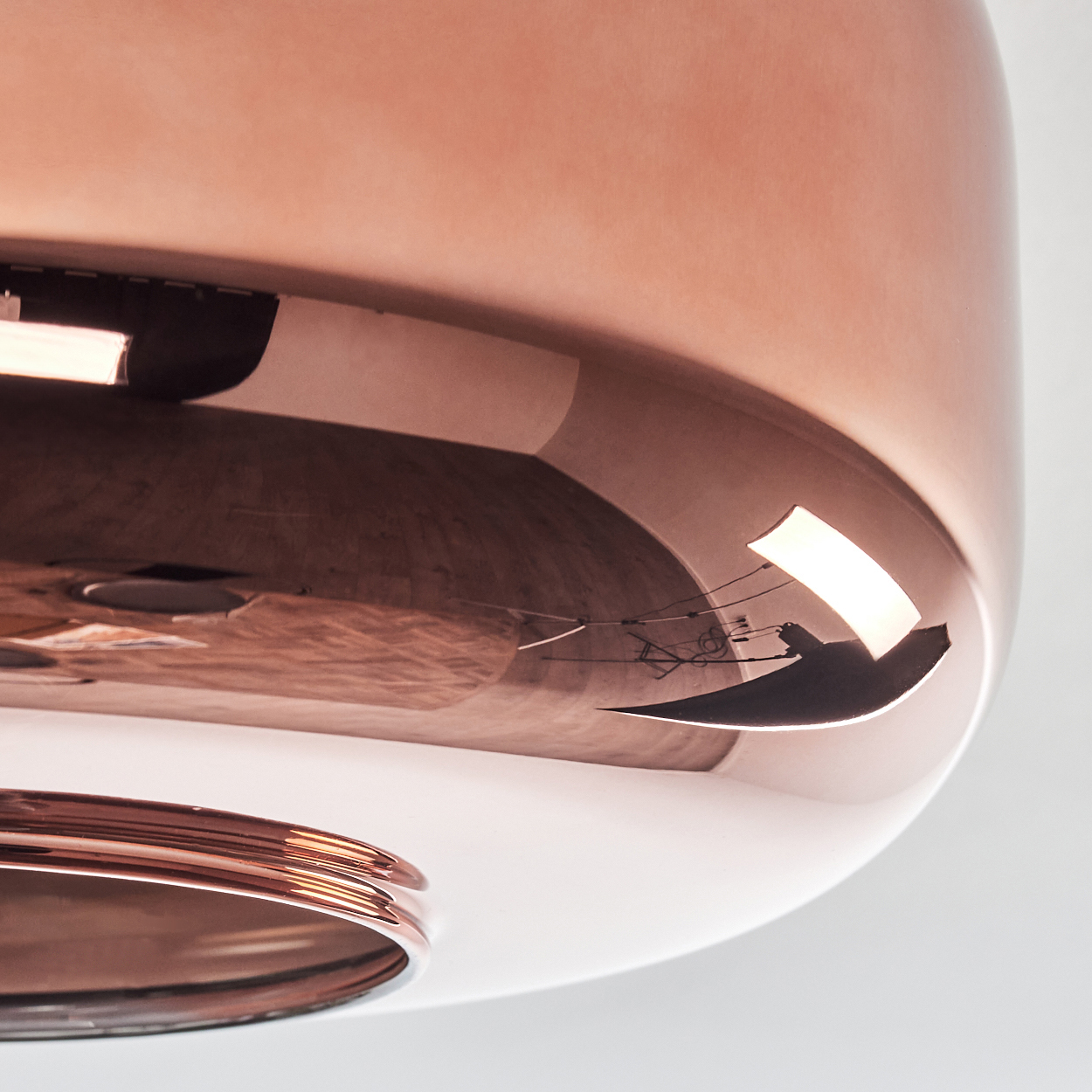 Nahaufnahme einer kupferfarbenen, reflektierenden Lampe. Die Oberfläche reflektiert ein Licht und andere Formen. Der untere Teil ist sichtbar.