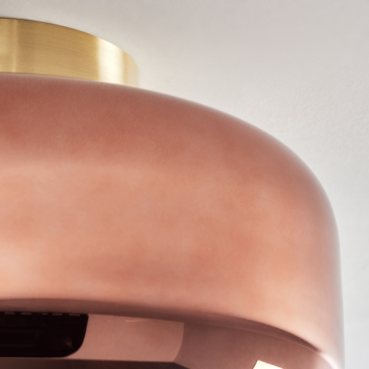 Nahaufnahme einer kupferfarbenen Leuchte. Oben befindet sich ein goldfarbener Ring. Der Hintergrund ist eine weiße Decke.