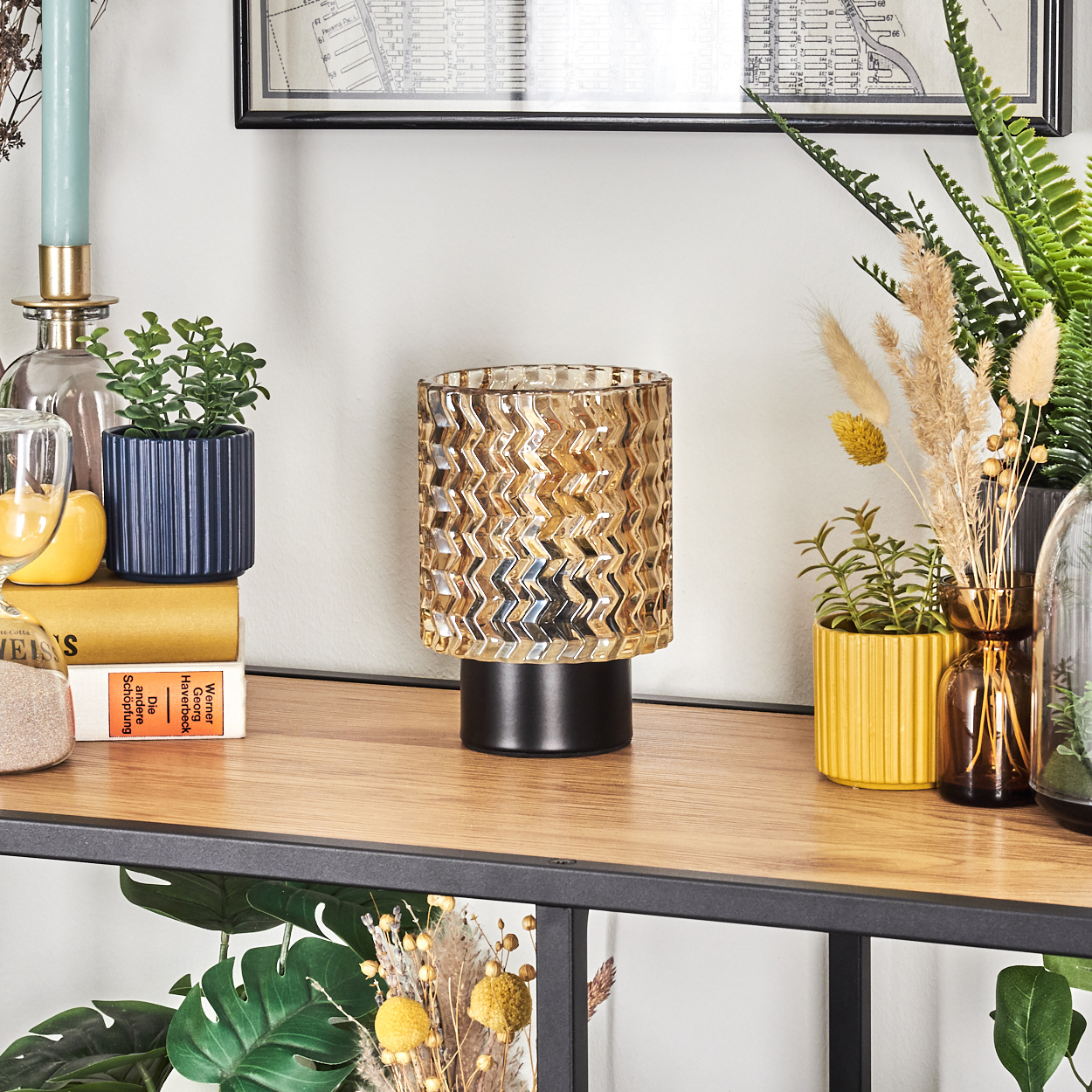 Ein dekoratives Regal mit einer Lampe, Pflanzen und Büchern. Die Lampe hat einen strukturierten goldenen Schirm und einen schwarzen Sockel.