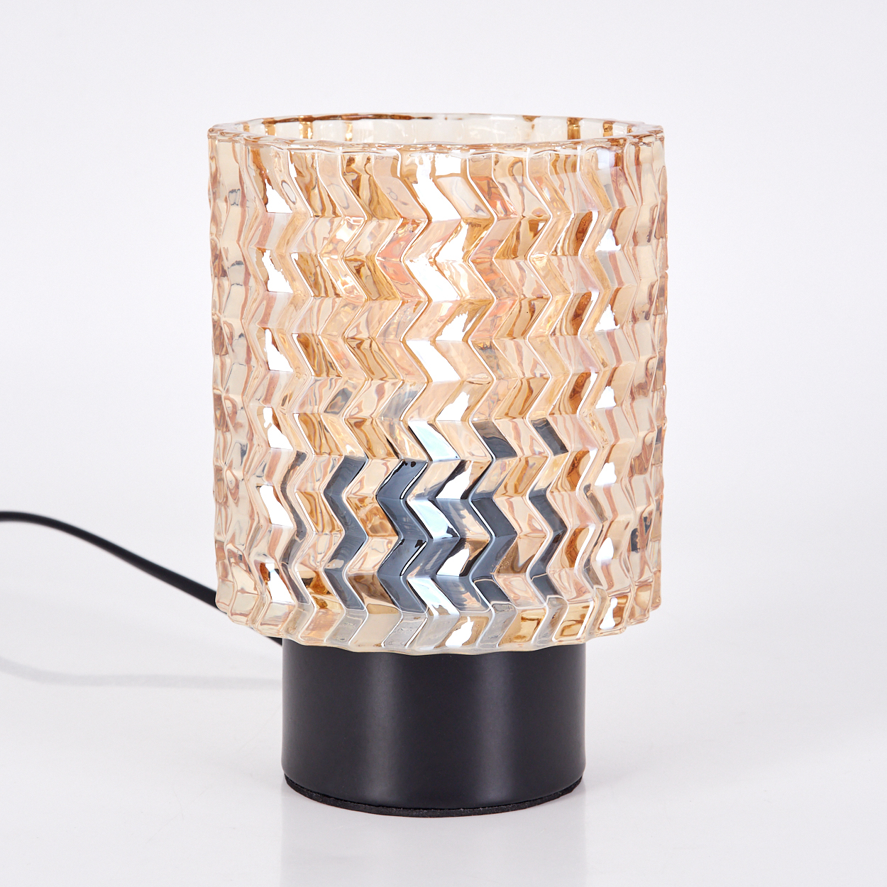 Eine dekorative Lampe mit gemustertem Glasschirm steht auf einem schwarzen Sockel. Ein schwarzes Netzkabel geht von der Lampe aus.