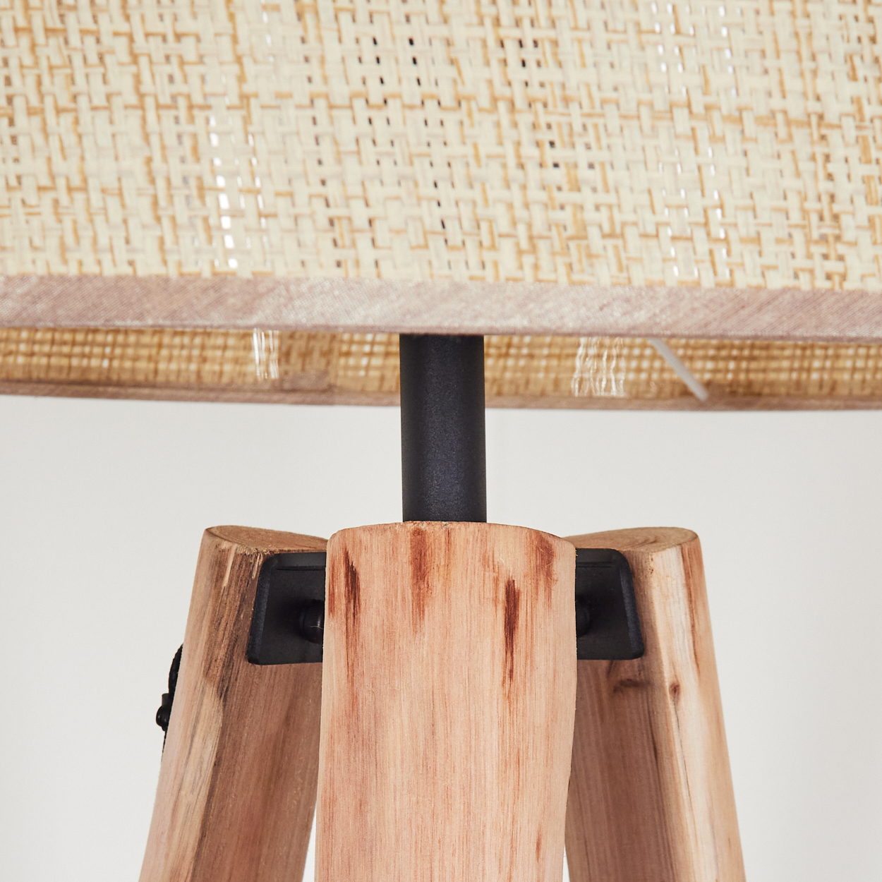 Nahaufnahme einer hölzernen Stativlampe. Der Lampenschirm ist aus gewebtem beigem Material. Die Beine sind aus hellfarbigem Holz, mit schwarzem Metallpfosten.