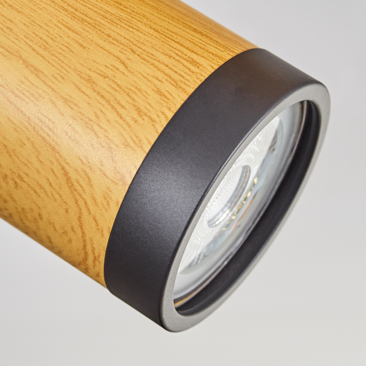 Nahaufnahme einer Holzlampe. Die Lampe hat einen schwarzen Ring um die Lichtquelle. Der Hintergrund ist weiß.