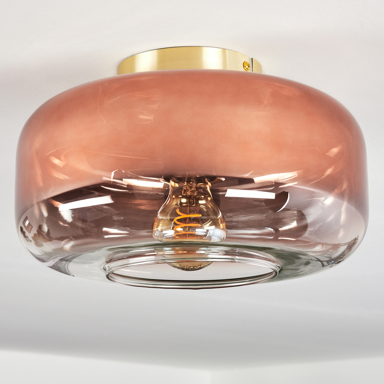 Eine Deckenleuchte. Sie hat eine klare Glasbasis und einen kupferfarbenen Glasschirm. Ein goldfarbenes Metallstück sitzt darüber.